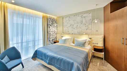 Et hotellrom med en dobbeltseng, blått sengeteppe og dekorativ vegg bak sengen. (AI-generert tekst)