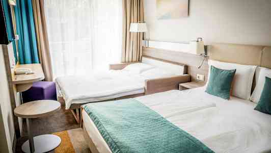 To senger i et hotellrom, med en stor vindusvegg og gardiner. (AI-generert tekst)