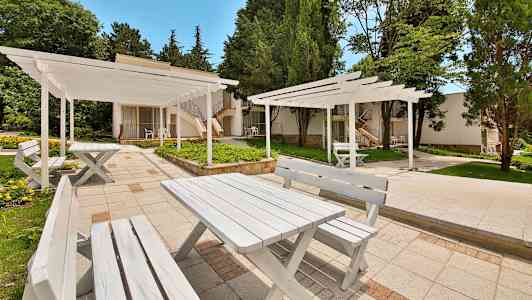 Hvite bord og benker utendørs omgitt av grøntområde. (AI-generert tekst)