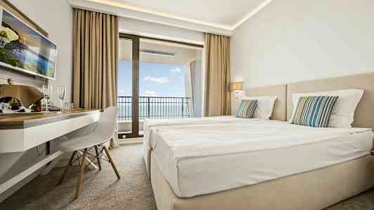 Hotellrom med to senger, skrivebord og balkong med utsikt over havet. (AI-generert tekst)