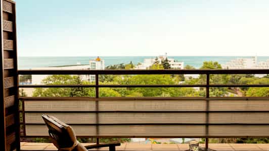 Utsikt fra en balkong over grøntområder, bygninger og havet. (AI-generert tekst)