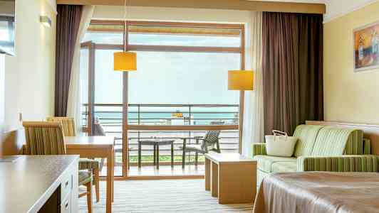 Et hotellrom med sittegruppe, bord, seng og balkong med utsikt. (AI-generert tekst)