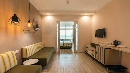 Et hotellrom med en sittebenk, bord, TV og en seng i bakgrunnen. (AI-generert tekst)