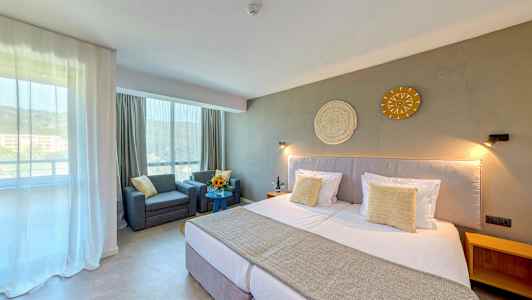 Et hotellrom med en stor seng, to lenestoler ved et bord og dekorasjon på veggen. (AI-generert tekst)