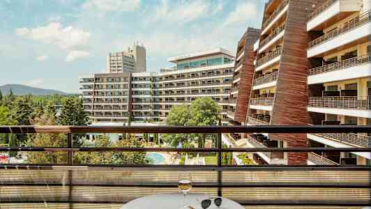 Utsikt fra en balkong med bord og glass over hotellbygninger og bassengområde. (AI-generert tekst)