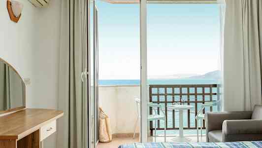 Hotellrom med åpen balkongdør og havutsikt. (AI-generert tekst)