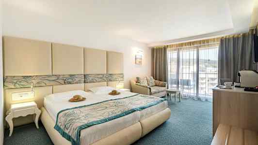 Hotellrom med dobbeltseng, sofa og balkong. (AI-generert tekst)