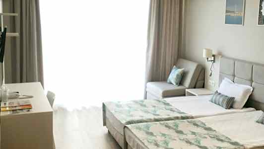 Lyst rom med to enkeltsenger, en sofa og skrivebord. (AI-generert tekst)