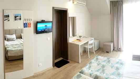 Et hotellrom med to senger, et skrivebord, kjøleskap og en veggmontert TV. (AI-generert tekst)