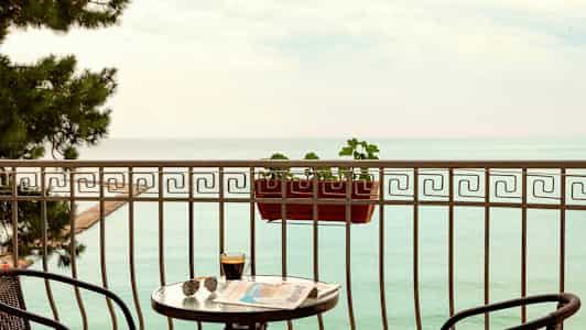 En balkong med utsikt over havet, med et bord, stoler og en blomsterkasse. (AI-generert tekst)