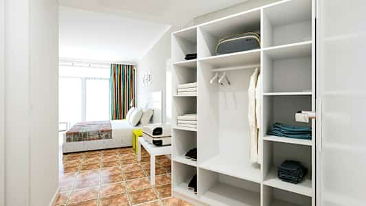 Hotellrom med seng og åpen garderobe, lyst og moderne innredet. (AI-generert tekst)