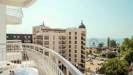 Utsikt fra en balkong over et hotellområde med et pariserhjul og havet i bakgrunnen. (AI-generert tekst)