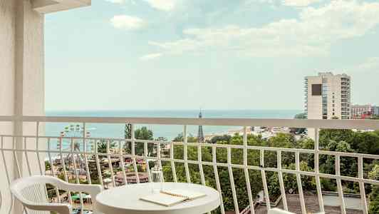 Utsikt fra balkong med bord og to stoler, hav og byer i bakgrunnen. (AI-generert tekst)