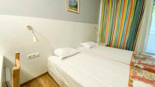 Et hotellrom med to enkeltsenger, en lysgrå vegg med et maleri over, og fargerike gardiner på siden. (AI-generert tekst)