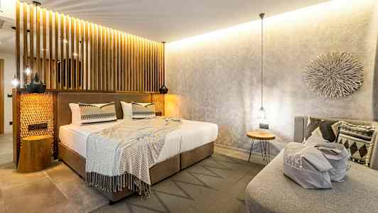 Soverom med moderne innredning, dobbeltseng med nøytrale laken og dekorative puter, samt en sofa med en veske plassert oppå. (AI-generert tekst)