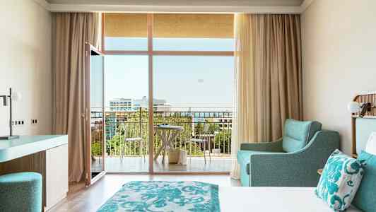 Hotellrom med dobbeltseng, turkis innredning og balkong med utsikt. (AI-generert tekst)