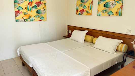 Et hotellrom med to enkeltsenger, hvite sengetøy og fargerike malerier på veggen. (AI-generert tekst)