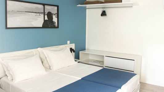 Hotellrom med to enkeltsenger, hvite vegger og en blå kontrastvegg. (AI-generert tekst)