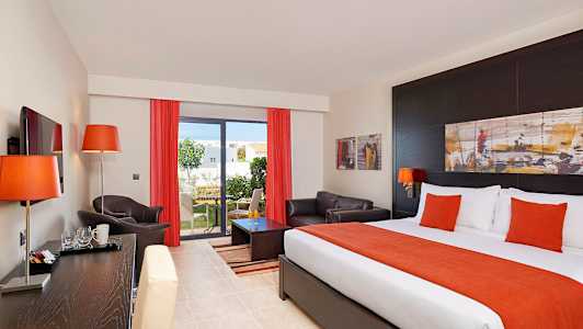 Hotellrom med seng, sofa og utsikt mot en hage. (AI-generert tekst)