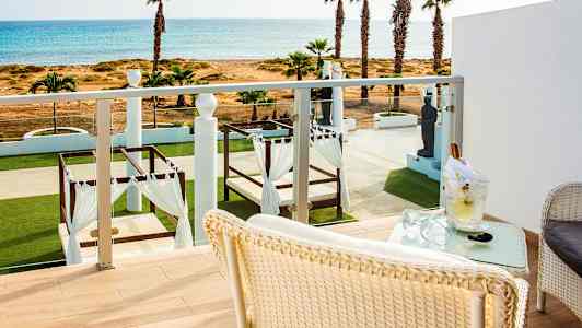 Utsikt fra en balkong mot en frodig hage med senger under baldakiner og havet i bakgrunnen. (AI-generert tekst)