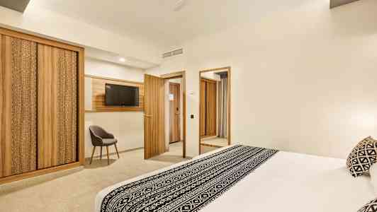 Et hotellrom med en stor seng dekorert med svart-hvitt mønster, tredetaljer i møbler og interiør inkludert garderober, dører og en TV-ramme. (AI-generert tekst)