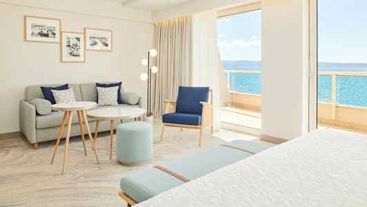 Lyst og moderne hotellrom med sittegruppe og utsikt mot havet. (AI-generert tekst)