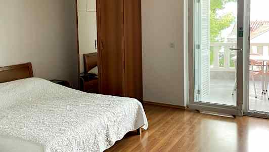 Et soverom med dobbeltseng, skap i tre og glassdør som fører til balkongen. (AI-generert tekst)