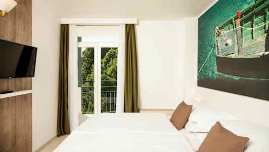 Et hotellrom med en dobbeltseng, en veggmontert TV og et stort vindu med grønne gardiner. (AI-generert tekst)