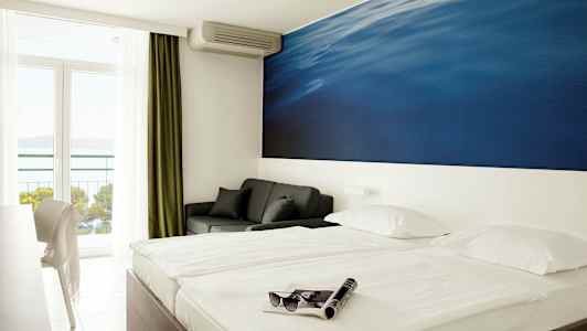 Dobbeltrom med stort blått veggmaleri bak sengen. Balkong med havutsikt. (AI-generert tekst)