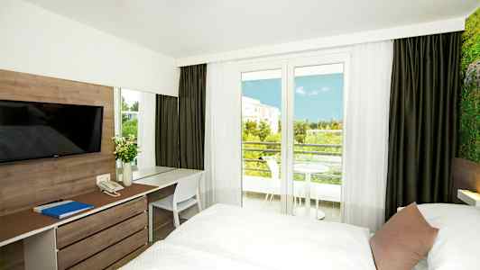 Hotellrom med to senger, skrivebord og utsikt mot balkongen og grøntområder. (AI-generert tekst)