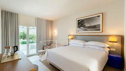 Soverom med dobbeltseng, nattbord, bilde på veggen og balkong med utsikt. (AI-generert tekst)