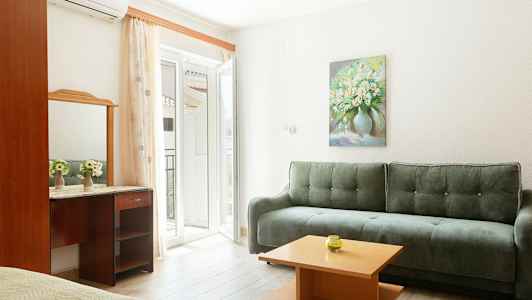 Et lyst interiør med en grønn sofa, et lite trebord og et speil over et skrivebord. Et maleri av blomster henger på veggen. (AI-generert tekst)