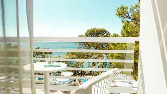 Utsikt fra en balkong over et basseng og havet med trær i forgrunnen. (AI-generert tekst)