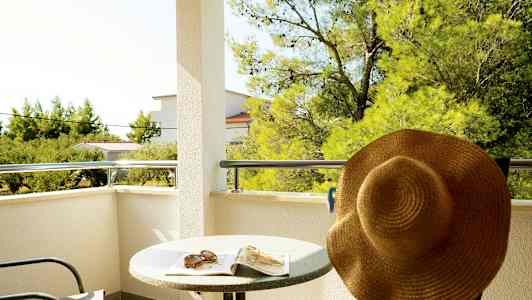 Balkong med bord, stol og solhatt, med utsikt til trær og bygninger. (AI-generert tekst)