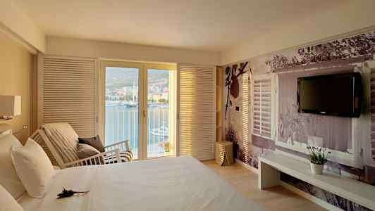 Soverom med utsikt over havet gjennom glassdører, en seng og en vegg med dekorativ fotografering. (AI-generert tekst)