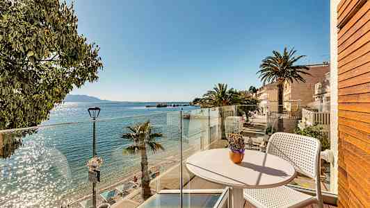 Utsikt fra en balkong mot en solfylt strand med palmer og klart vann. (AI-generert tekst)