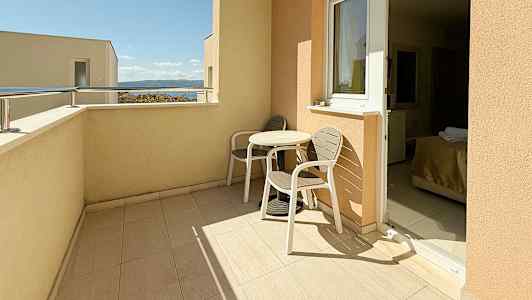 En balkong med to stoler og et bord, med utsikt mot himmelen og havet. (AI-generert tekst)