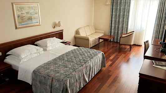 Et hotellrom med en dobbeltseng, sofa, trebord og stoler samt et skrivebord med TV. (AI-generert tekst)