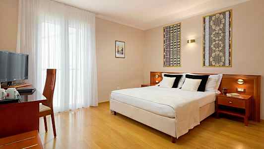 Et hotellrom med en dobbeltseng, et skrivebord og en stol samt en TV. (AI-generert tekst)