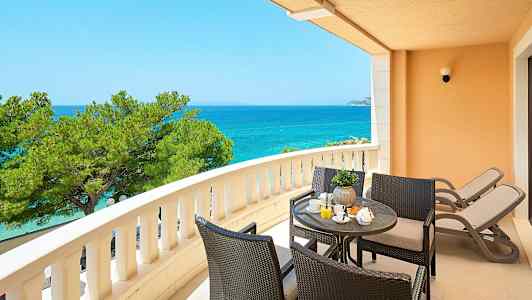 En balkong med utsikt over havet, sittegruppe og to solstoler. (AI-generert tekst)