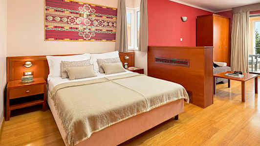 Hotellrom med en dobbeltseng, nattbord og kunst på veggen. (AI-generert tekst)