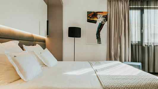 Moderne hotellrom med en stor seng, kunstverk på veggen og et vindu med lyse gardiner. (AI-generert tekst)