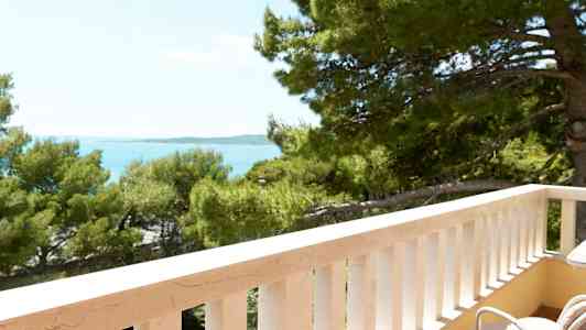 Utsikt fra en balkong med hvite rekkverk mot trær og hav. (AI-generert tekst)