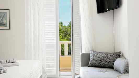 Et hotellrom med en sofa, en seng og en balkongdør som fører ut til utsikt over trær. (AI-generert tekst)