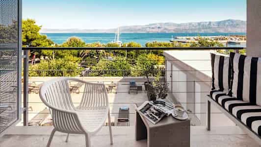 Utsikt fra en terrasse med møbler, utsikt mot havet og fjell. (AI-generert tekst)
