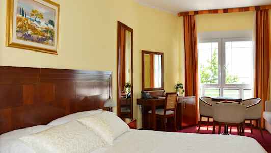 Et hotellrom med en dobbeltseng, skrivebord, stoler og et vindu. (AI-generert tekst)