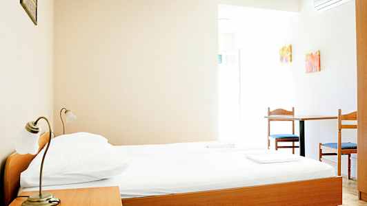 Et enkelt hotellrom med en seng av tre, et nattbord og et bord med to stoler. (AI-generert tekst)