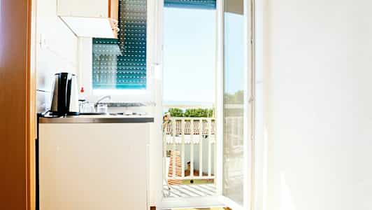 Et lite kjøkken med utsikt mot en balkong og havet i bakgrunnen. (AI-generert tekst)