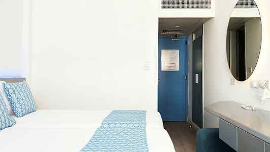 Hotellrom med to senger, blå detaljer og skrivebord. (AI-generert tekst)