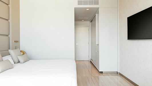 Et moderne hotellrom med en stor seng, hvit vegg, en dør og en veggmontert TV. (AI-generert tekst)